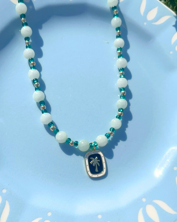 Necklace with white beads and a palm tree pendant on a light blue plate